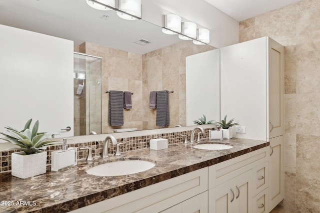 bathroom with a stall shower, double vanity, a sink, and tile walls