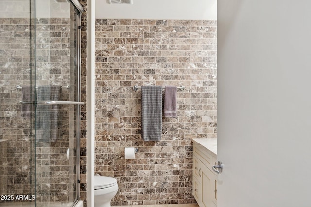full bath featuring tile walls, a shower stall, vanity, toilet, and visible vents