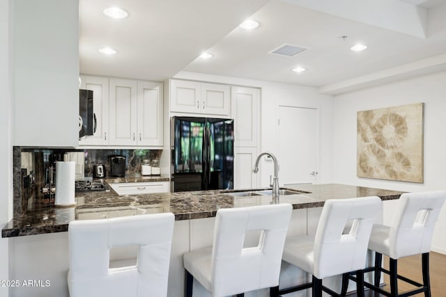 kitchen featuring a sink, decorative backsplash, white cabinetry, freestanding refrigerator, and wood finished floors