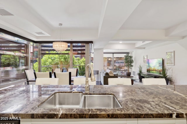 kitchen with dark stone countertops, an inviting chandelier, a sink, and visible vents