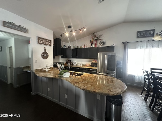 kitchen featuring ventilation hood, lofted ceiling, a breakfast bar area, stainless steel fridge, and kitchen peninsula