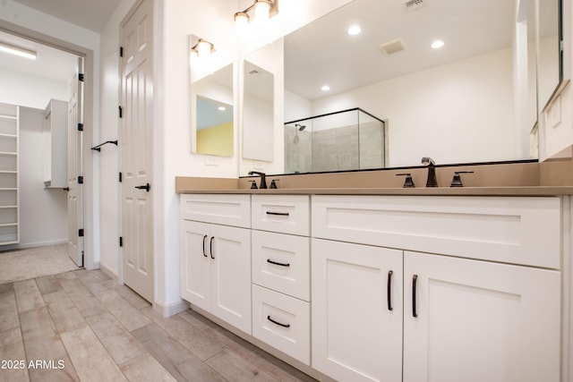 full bathroom with wood finish floors, a sink, visible vents, a shower stall, and double vanity