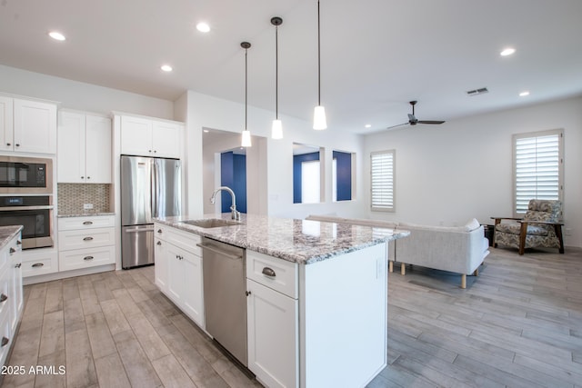 kitchen featuring appliances with stainless steel finishes, open floor plan, white cabinetry, a sink, and an island with sink