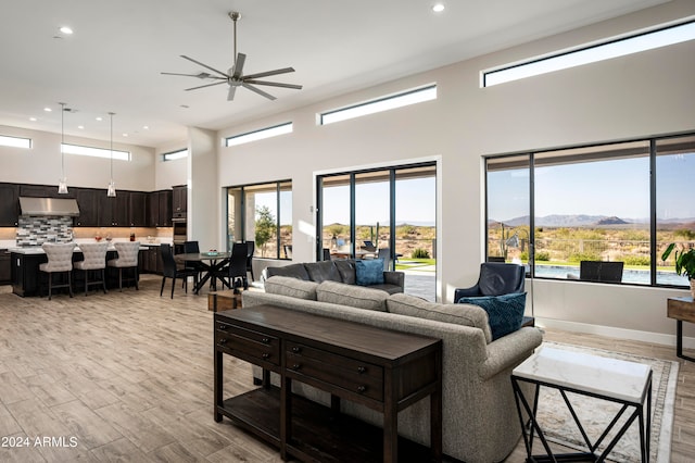 living room featuring light wood-type flooring, a mountain view, ceiling fan, and a towering ceiling