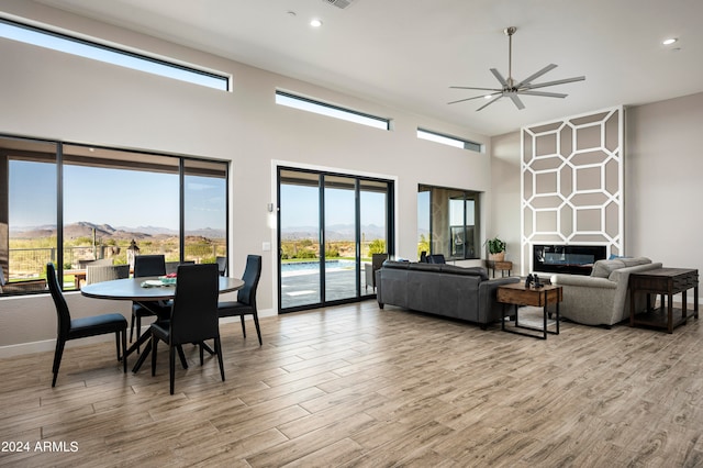 living room featuring ceiling fan, light wood-type flooring, a towering ceiling, and a large fireplace