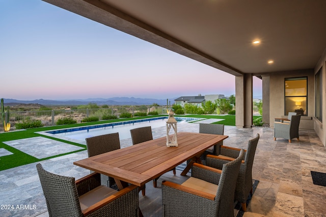 patio terrace at dusk with a fenced in pool and a mountain view