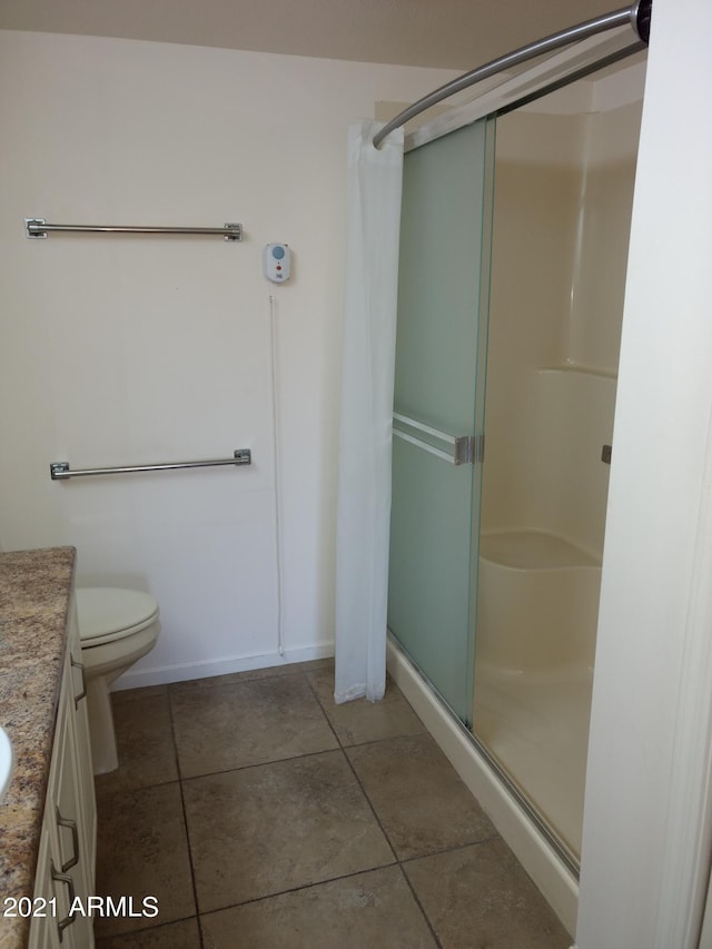 bathroom with a shower with door, vanity, tile patterned floors, and toilet