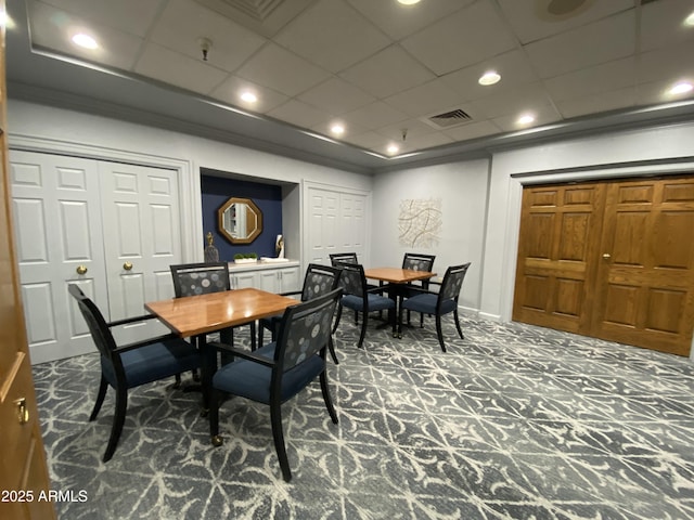 carpeted dining area with crown molding and a paneled ceiling