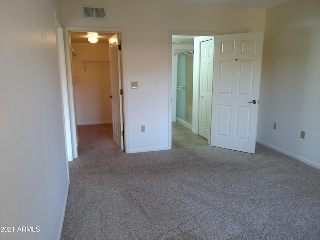 unfurnished bedroom with a walk in closet, light colored carpet, and a closet