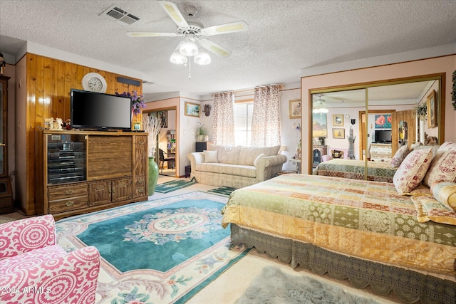 bedroom featuring ceiling fan, wooden walls, a closet, and a textured ceiling