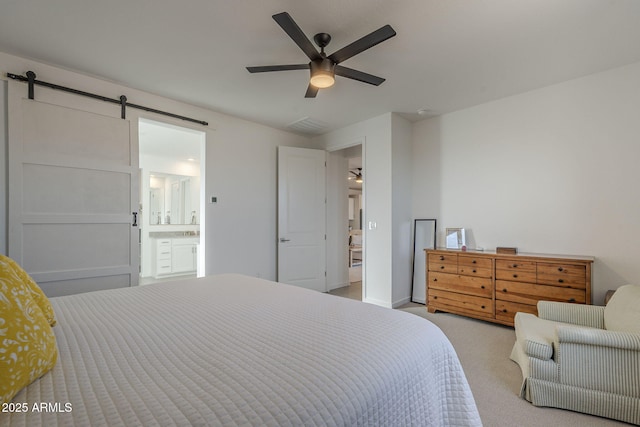 bedroom with ceiling fan, light colored carpet, connected bathroom, and a barn door