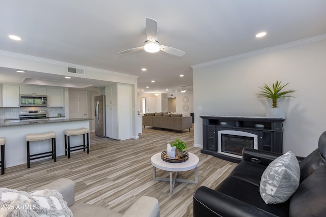 living room with ornamental molding, a premium fireplace, ceiling fan, and light wood-type flooring