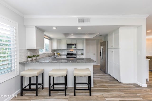 kitchen with a kitchen bar, appliances with stainless steel finishes, kitchen peninsula, light stone countertops, and backsplash