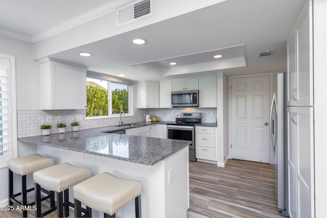 kitchen with appliances with stainless steel finishes, white cabinetry, sink, kitchen peninsula, and a raised ceiling