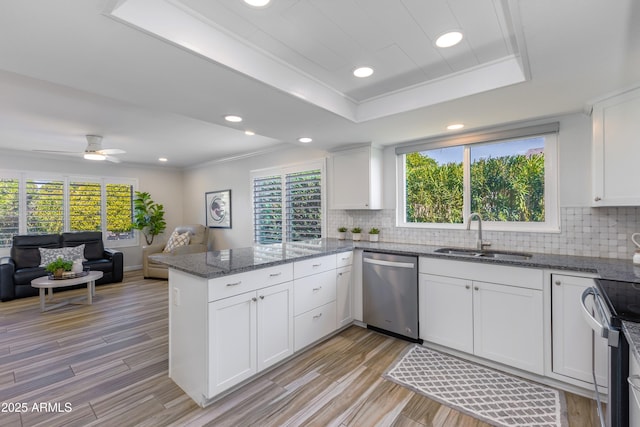 kitchen with appliances with stainless steel finishes, kitchen peninsula, white cabinetry, sink, and a tray ceiling