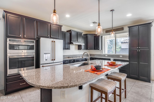 kitchen featuring a kitchen breakfast bar, light stone counters, high end white refrigerator, a center island with sink, and double oven