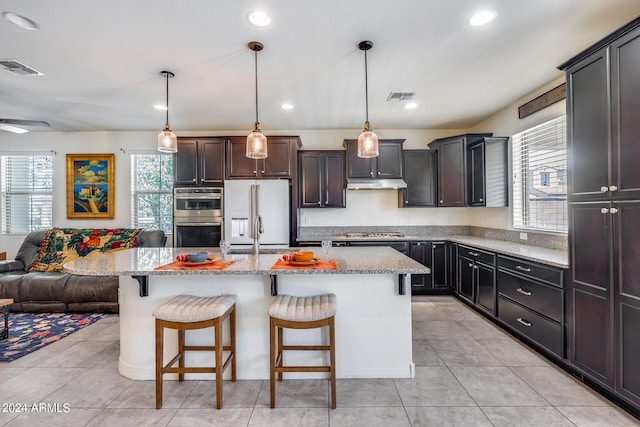 kitchen featuring hanging light fixtures, a kitchen island, stainless steel appliances, a kitchen bar, and sink