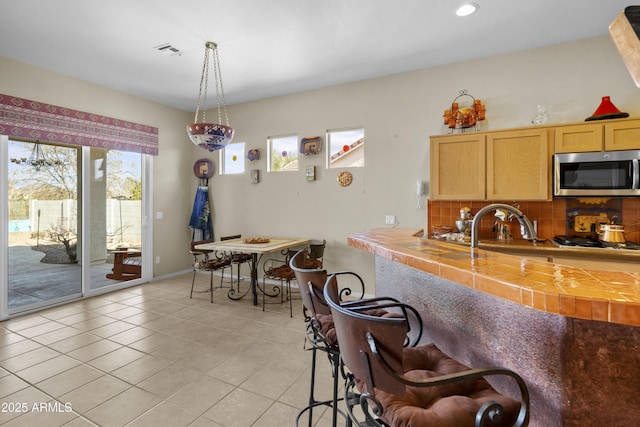 kitchen with light brown cabinetry, tasteful backsplash, decorative light fixtures, tile countertops, and stainless steel appliances