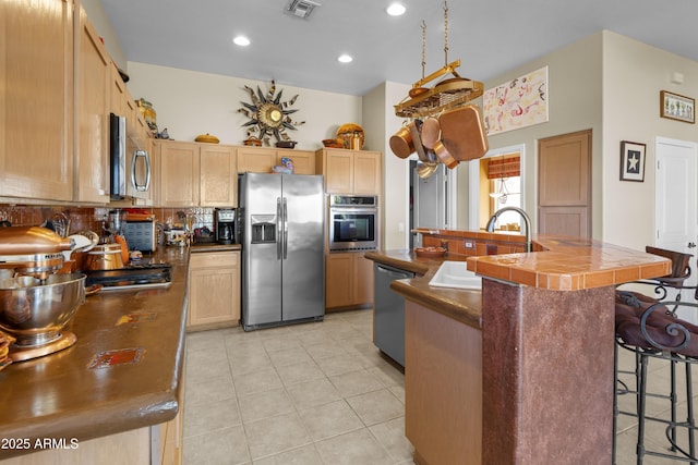 kitchen with sink, a breakfast bar, stainless steel appliances, a center island with sink, and light brown cabinetry