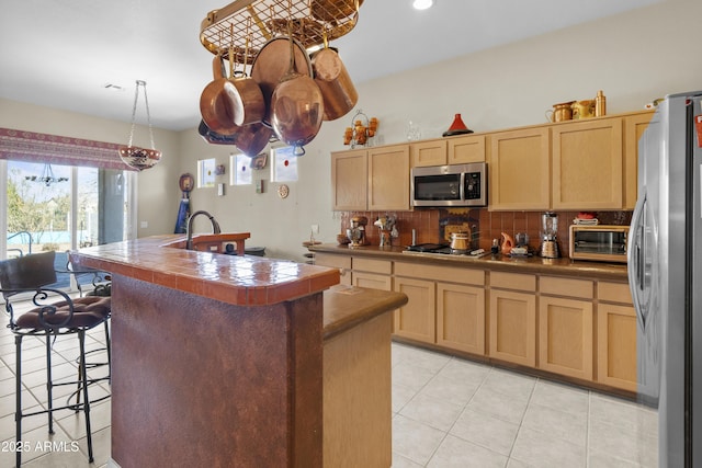 kitchen with light brown cabinetry, backsplash, tile counters, and stainless steel appliances