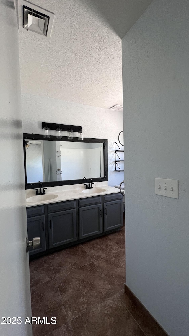 full bathroom with double vanity, a textured ceiling, and baseboards