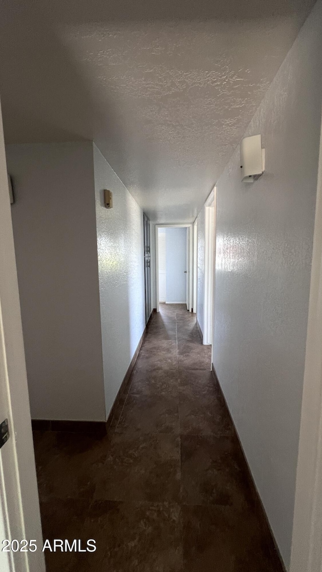 hall with unfinished concrete flooring, a textured ceiling, and baseboards