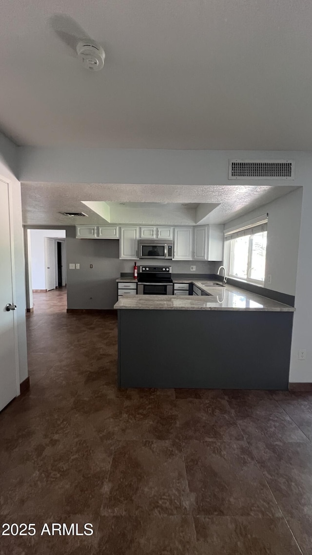 kitchen featuring appliances with stainless steel finishes, a peninsula, a sink, white cabinetry, and baseboards