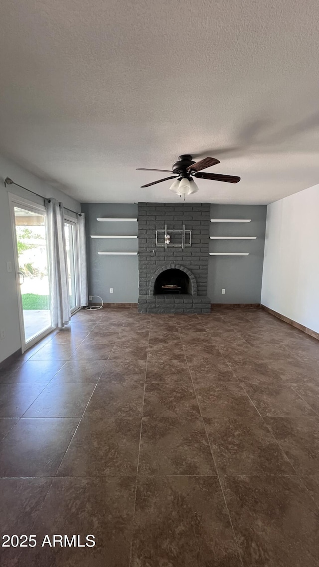 unfurnished living room featuring ceiling fan, a textured ceiling, a brick fireplace, and baseboards