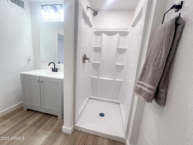 full bath featuring vanity, visible vents, wood finished floors, a textured wall, and baseboards