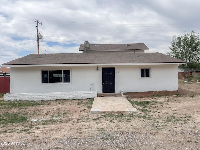 back of property with roof with shingles, stucco siding, and fence