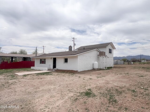 rear view of house featuring a chimney, a mountain view, stucco siding, and fence