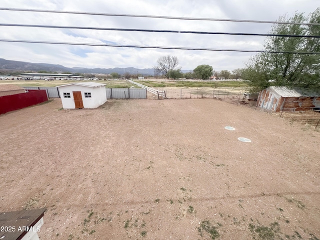 view of yard featuring a storage shed, a mountain view, fence, and an outdoor structure