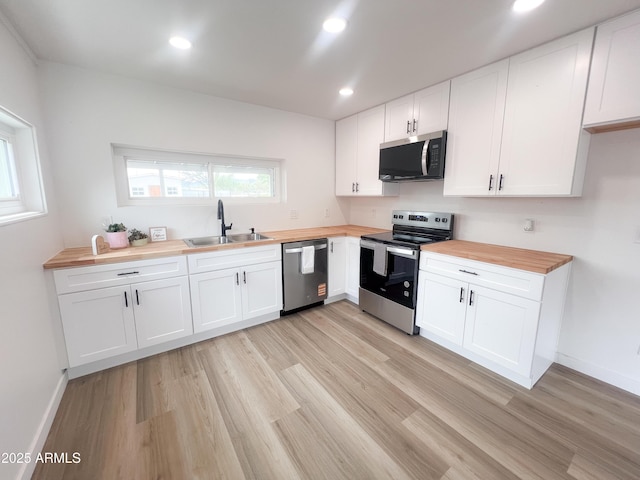 kitchen featuring a sink, light wood finished floors, wood counters, white cabinetry, and stainless steel appliances