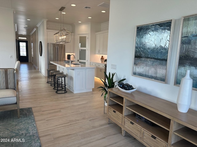 interior space featuring white cabinets, a kitchen island with sink, light hardwood / wood-style flooring, and decorative light fixtures