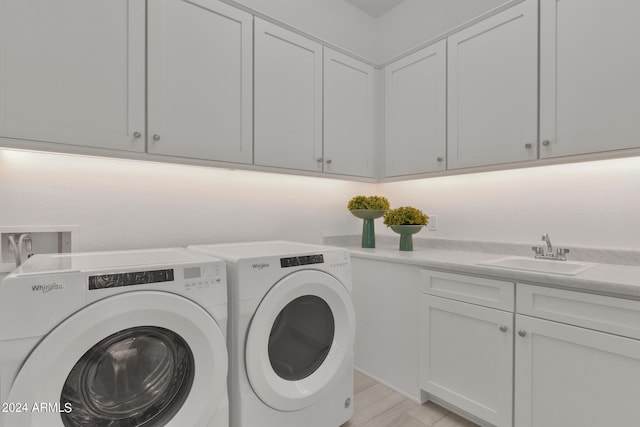 clothes washing area with light hardwood / wood-style floors, sink, washer and dryer, and cabinets