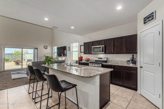 kitchen featuring a kitchen island with sink, sink, light colored carpet, stainless steel appliances, and light stone countertops