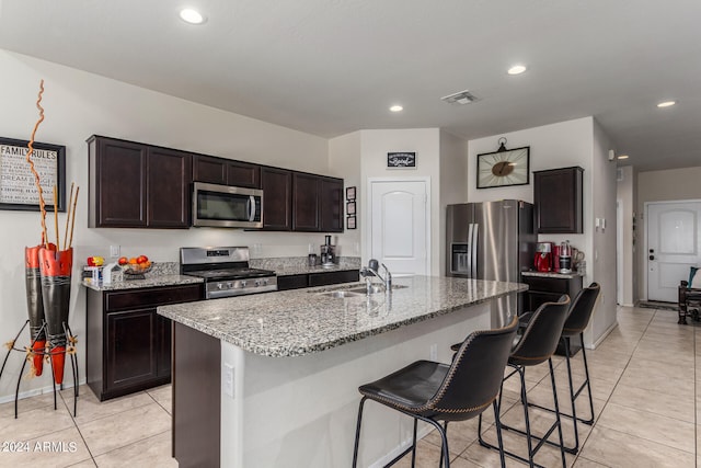 kitchen featuring a kitchen breakfast bar, stainless steel appliances, dark brown cabinetry, a center island with sink, and sink