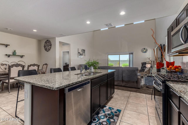 kitchen with a breakfast bar area, light tile patterned floors, stainless steel appliances, a kitchen island with sink, and sink