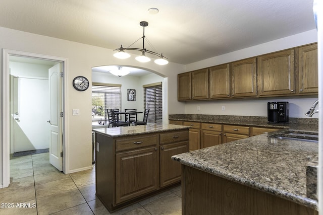 kitchen featuring sink, decorative light fixtures, a kitchen island, dark stone countertops, and light tile patterned flooring