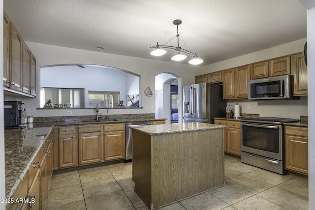 kitchen with appliances with stainless steel finishes, a center island, brown cabinetry, and light tile patterned floors