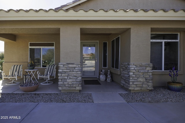 property entrance with a porch, stone siding, a tiled roof, and stucco siding