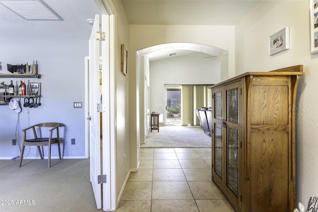 hall featuring arched walkways, light tile patterned floors, light colored carpet, visible vents, and baseboards