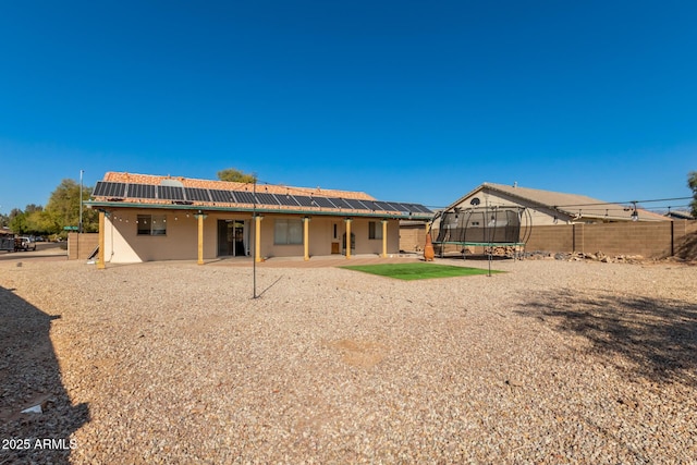 rear view of property with a trampoline, a patio area, and solar panels