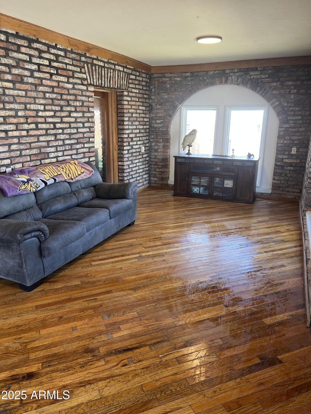 living area featuring wood finished floors, brick wall, and arched walkways