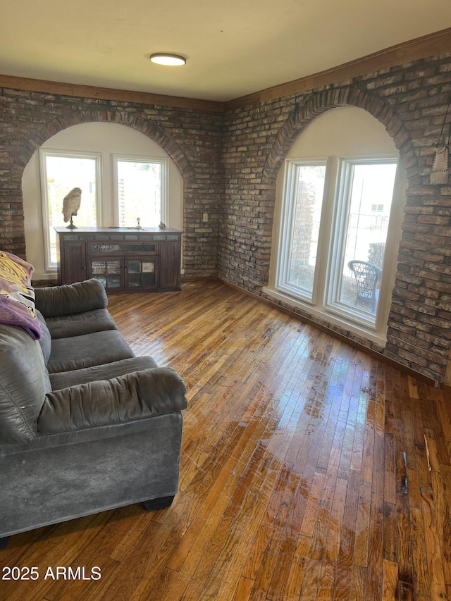 living room featuring arched walkways, hardwood / wood-style floors, and brick wall