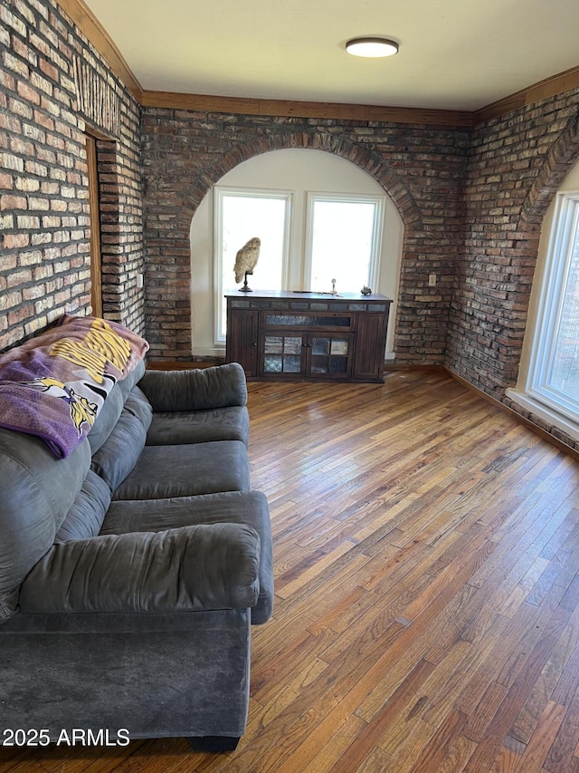 living area with a healthy amount of sunlight, brick wall, hardwood / wood-style flooring, and arched walkways