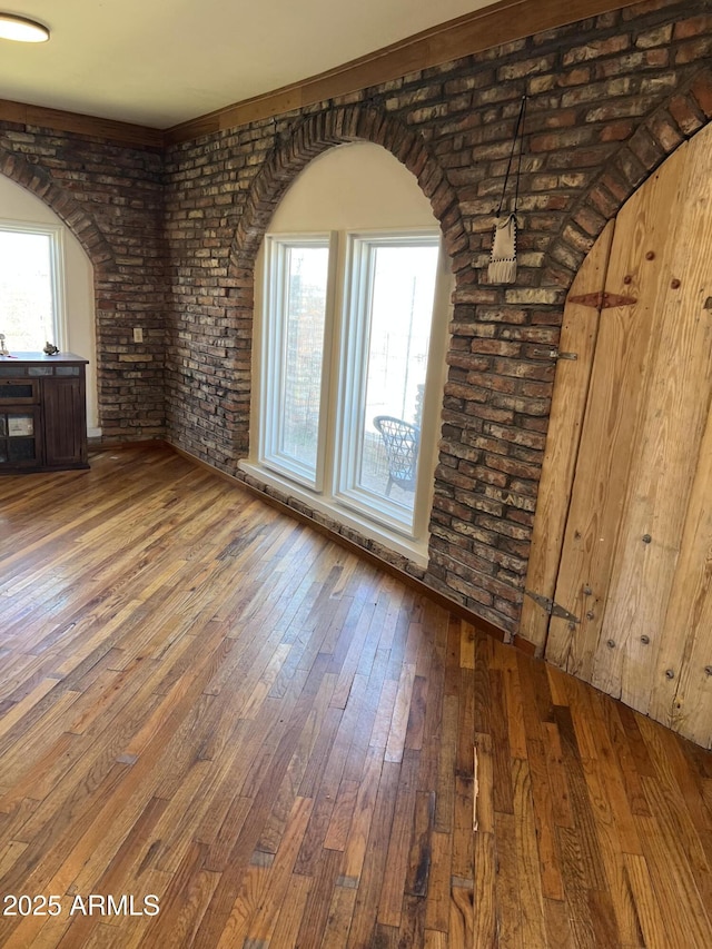 unfurnished living room featuring wood-type flooring, arched walkways, and brick wall