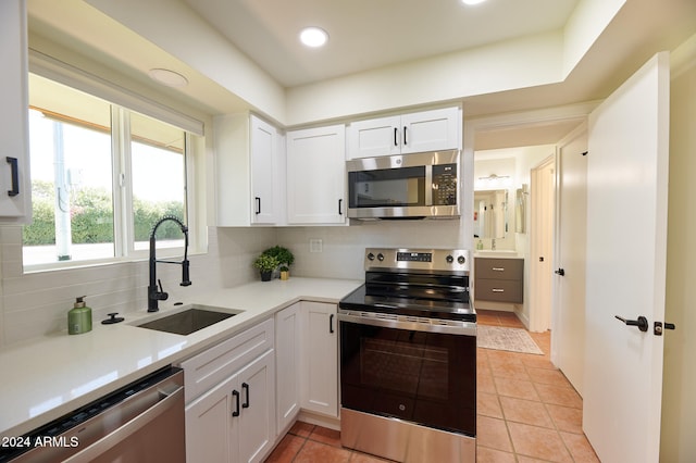 kitchen featuring tasteful backsplash, sink, light tile patterned floors, stainless steel appliances, and white cabinets