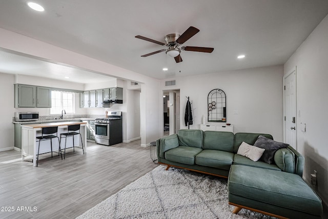 living room featuring ceiling fan, light hardwood / wood-style floors, and sink