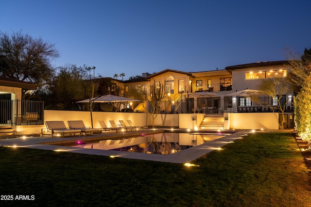 back house at dusk featuring a yard and a patio